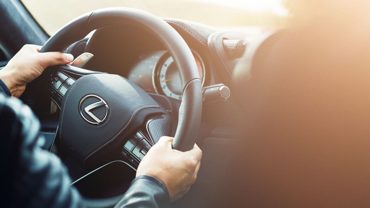 A person with their hand on a Lexus steering wheel