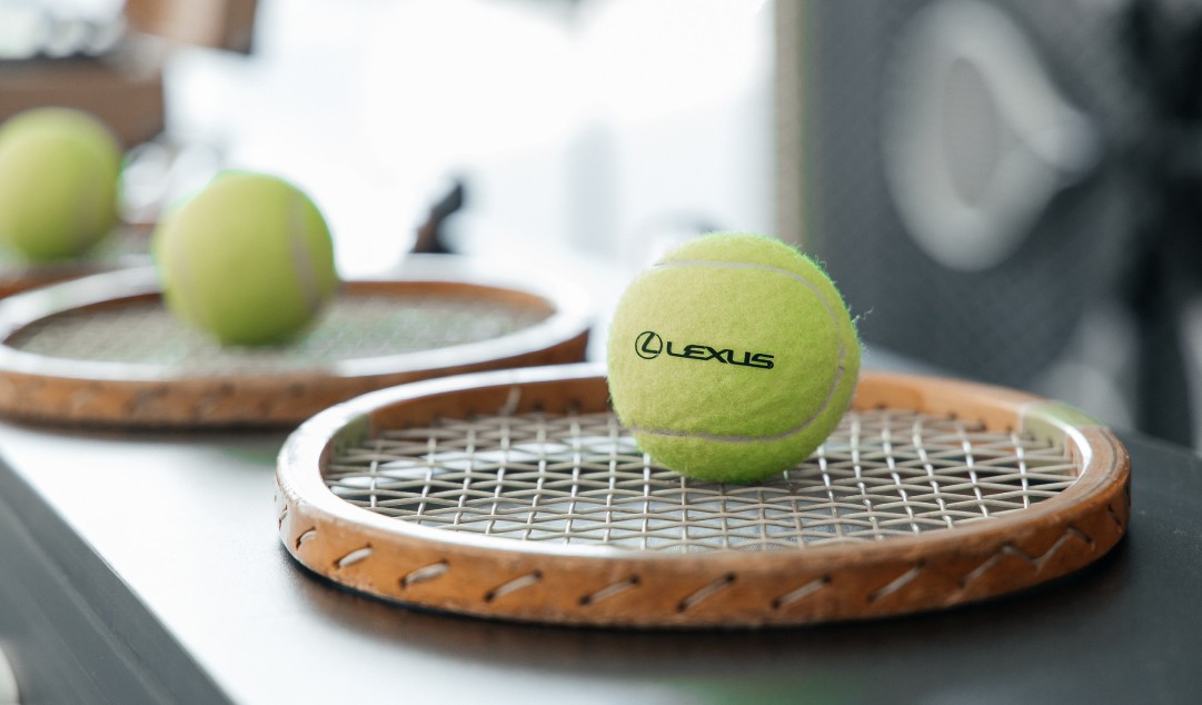 A tennis ball with the Lexus logo on, sat on a tennis racket